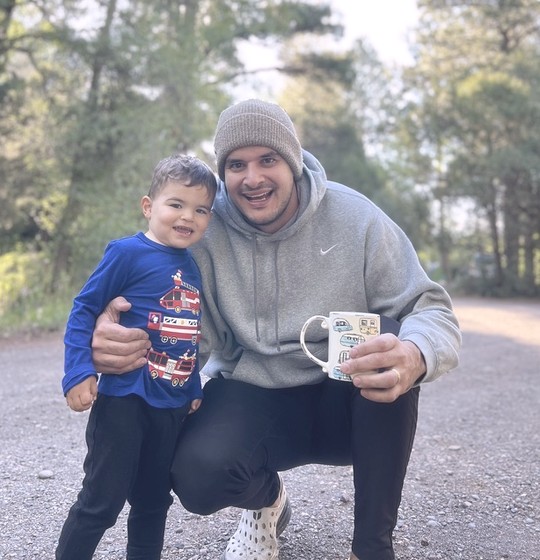 Simon crouching with his son and a coffee mug on a forest road